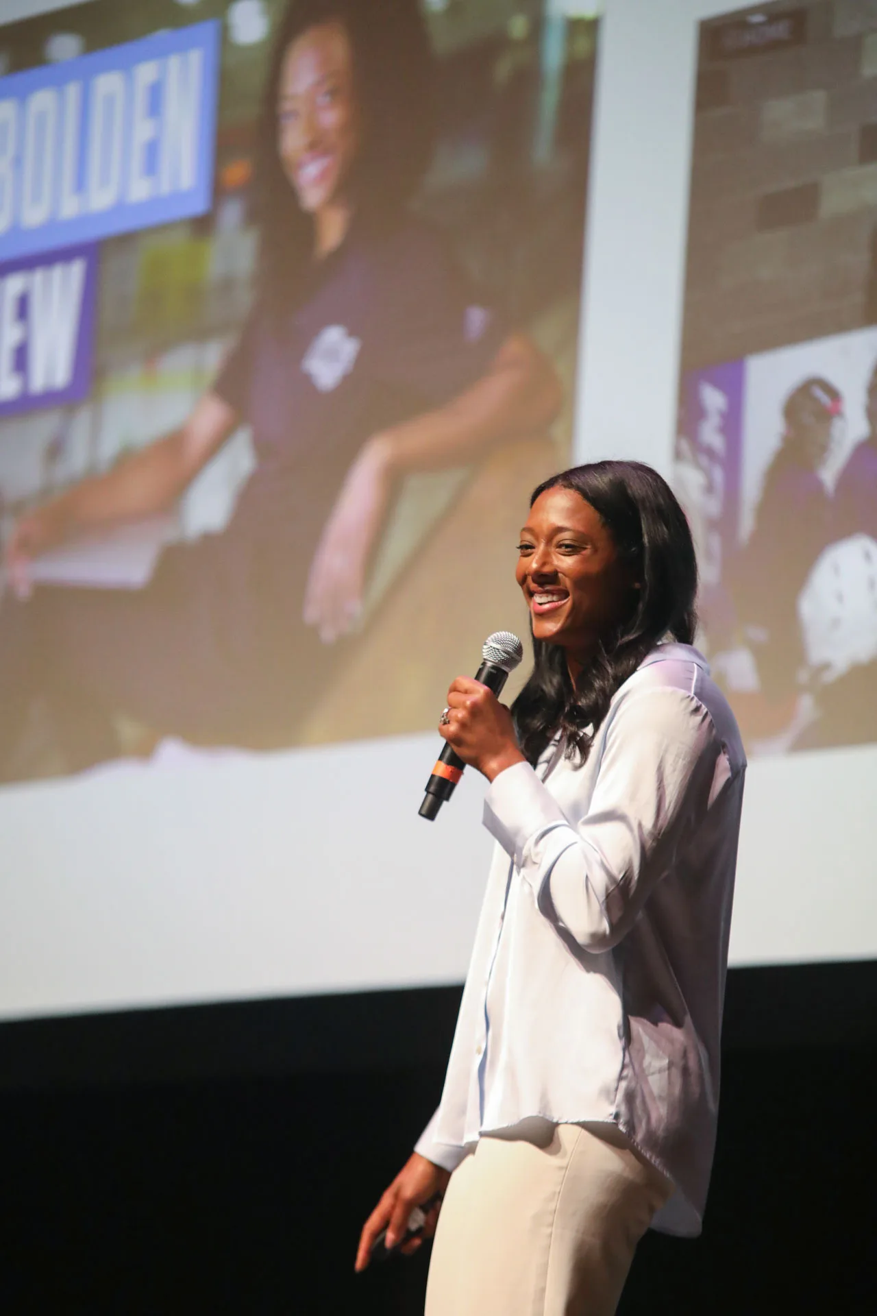 Blake Bolden on stage in a white blouse, smiling as she speaks into a microphone
